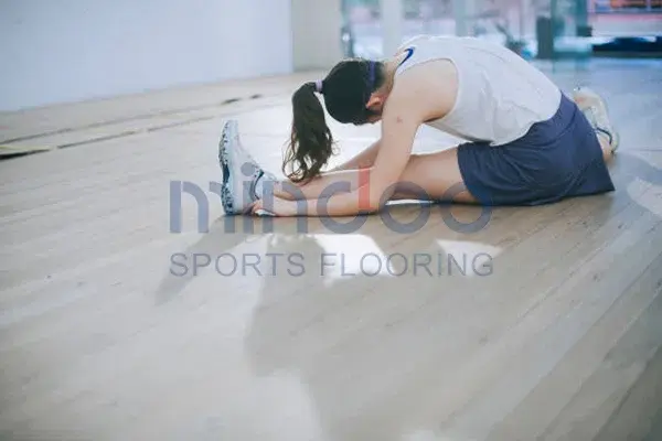 A girl doing leg stretches on a smooth gym wooden floor