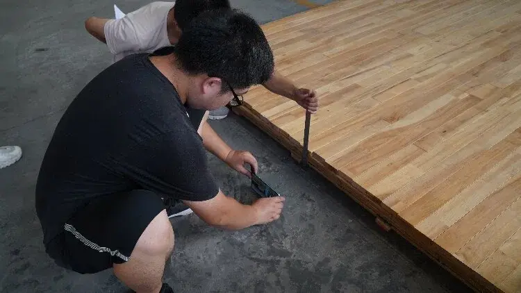 Staff members inspect the thickness of the sports wood flooring