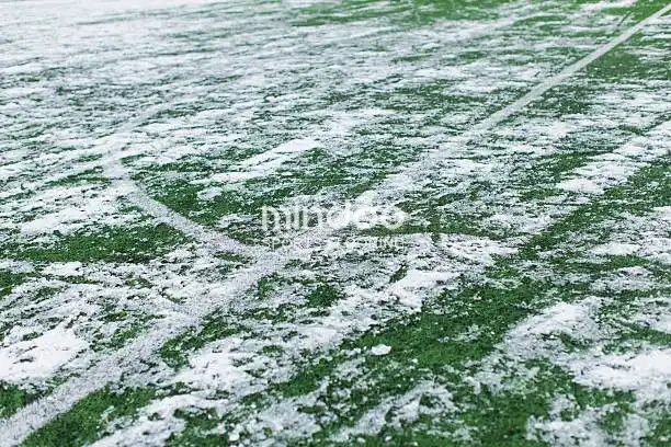The artificial turf of the football field is covered with snow